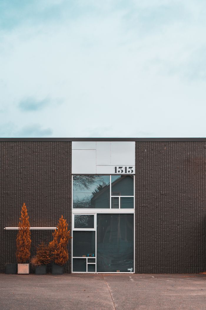 who-we-are A minimalist facade featuring geometric architecture and autumnal potted shrubs.